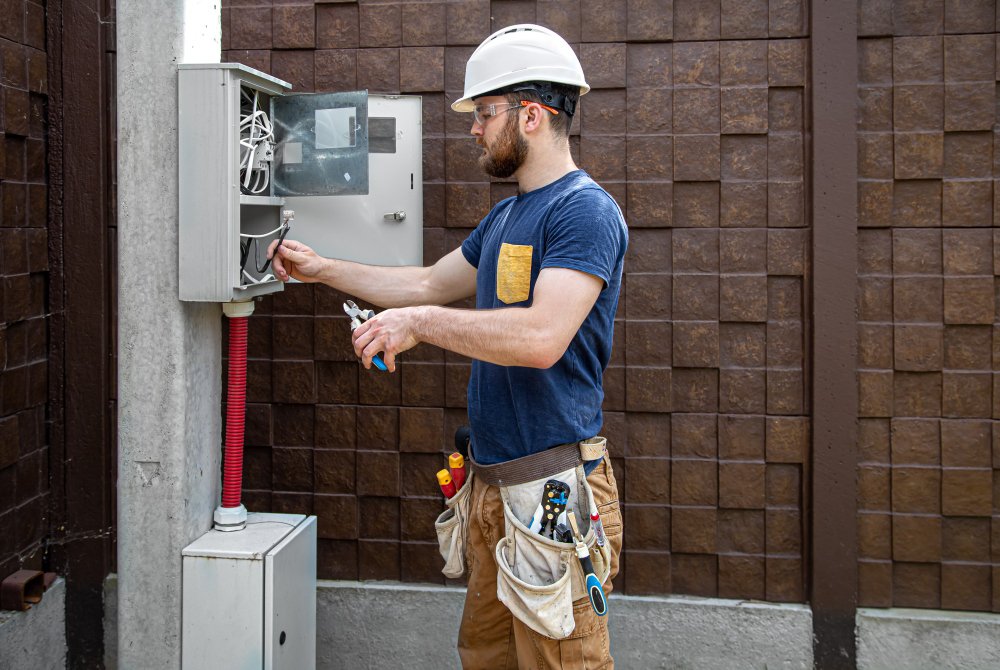 electrician-builder-work-examines-cable-connection-electrical-line-fuselage-industrial-switchboard-professional-overalls-with-electrician-s-tool